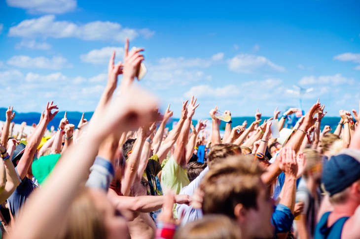 Teenagers at summer music festival under the stage in a crowd enjoying themselves, clapping and singing